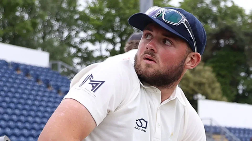 Tom Norton seated on the boundary with glasses on top of cap looks over his shoulder towards the stands at Sophia Gardens